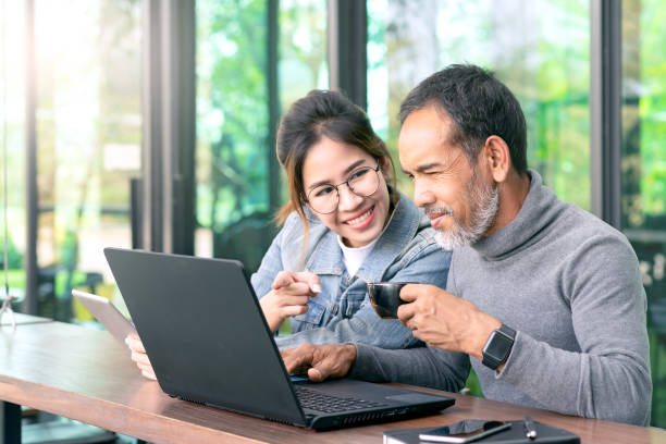 istock Attractive mature asian man with white stylish short beard looking at laptop computer with teenage eye glasses hipster woman in cafe. Teaching internet online or wifi technology in older man concept. 1131379064