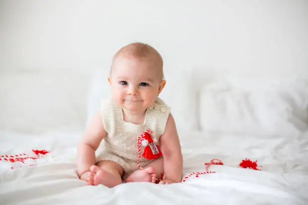 Photo of Cute baby toddler boy, playing with white and red bracelets