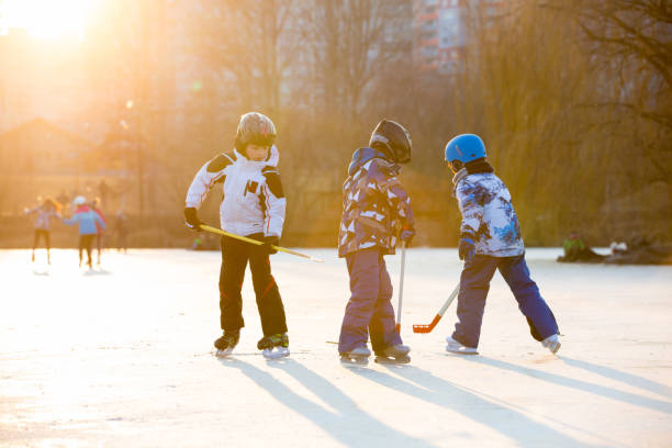 enfants, jouant au hockey et patinant dans le parc sur le lac gelé, heure d'hiver au coucher du soleil - ice hockey child childhood little boys photos et images de collection