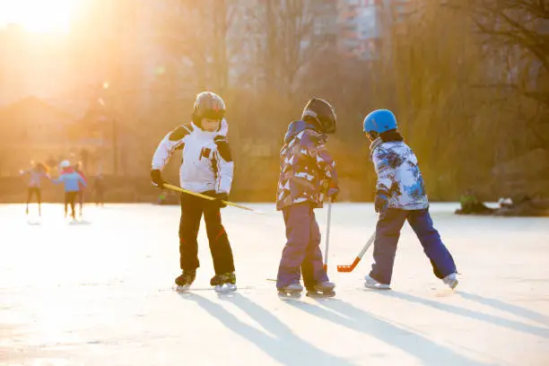 Photo of Children, playing hockey and skating in the park on frozen lake, wintertime on sunset