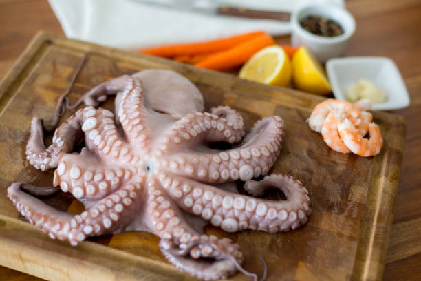 frischer tintenfisch auf schneidebrett mit zitrone, weißwein und pfeffer auf rustikalen holztisch - octopus tentacle isolated white stock-fotos und bilder