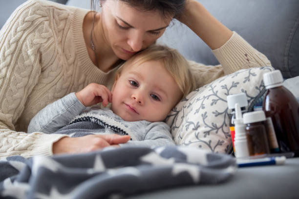 Sick child, toddler boy lying in bed with a fever, resting at home Sick child, toddler boy lying on the couch in living room with a fever, mom cheching his temperature, resting at home sick in babies stock pictures, royalty-free photos & images