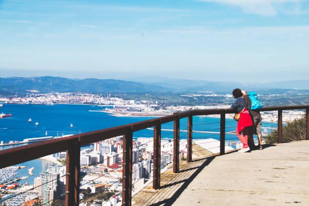 Two tourists looking at the awesome landscape from the Rock of Gibraltar Gibraltar, Gibraltar - February 9, 2019: Two tourists looking at the awesome landscape from the Rock of Gibraltar colony territory photos stock pictures, royalty-free photos & images