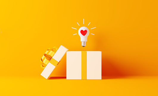 A light bulb with heart shape coming out of white gift box on yellow background. Horizontal composition with  copy space. Shopping and gift concept.