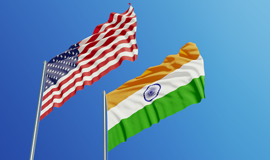 American and Indian flags are waving with over  blue sky. Low angle view. Dispute and conflict concept. Horizontal composition with copy space.