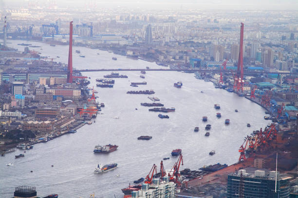 Countless nautical vessels float on the river. A bridge is crossing the river. Hazy day with smog