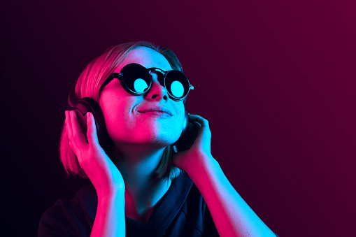 Happy pretty woman with headphones listening to music over red neon background at studio.