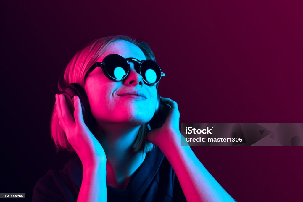 Fashion pretty woman with headphones listening to music over neon background Happy pretty woman with headphones listening to music over red neon background at studio. Music Stock Photo