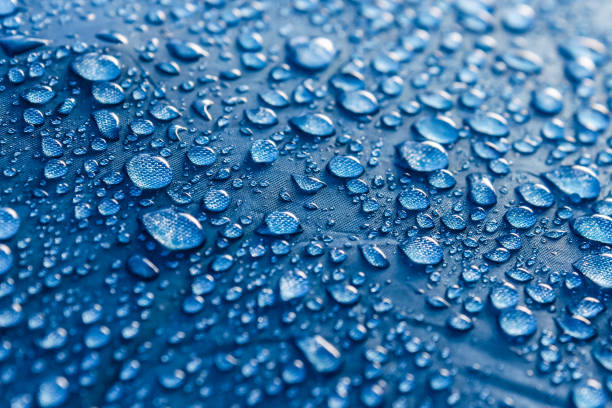 Water drops on the fabric. Rain Water droplets on blue fiber waterproof fabric. Water drops pattern over a waterproof cloth. Blue background. Dark blue rainproof tent sheet with morning rain drops. water repellent stock pictures, royalty-free photos & images