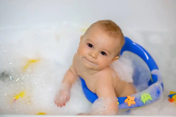 Photo of Little baby boy, playing with rubber ducks in bath tube