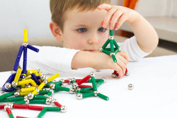 mignon petit enfant garçon jouant des aimants jouet pour le développement du cerveau, le concept de motricité fine et de créativité - magnet photos et images de collection