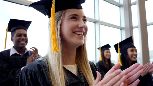Beautiful female high school graduate claps during graduation ceremony