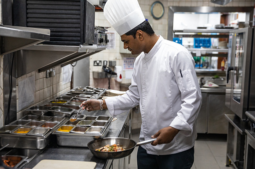 Chef in hotel or restaurant kitchen cooking, he is seasoning dishes