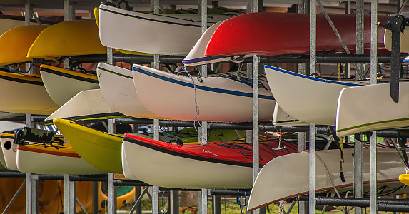 Various canoes have been stored in a steel rack. They are next to each other and stacked and are ready to be rented out to customers.