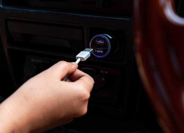 Vehicle interior view of a hand plugging in a USB cable to a USB in car dashboard 12v socket with selective focus stock photo