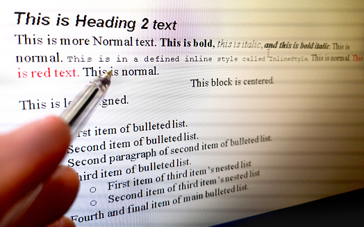hand with pen indicate text formatting rules on word processor software on computer screen .