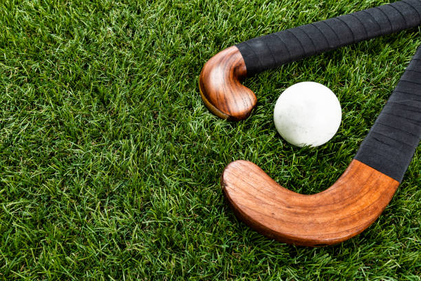 A pair of wooden field hockey stick with ball sitting on turf A high angle view of a pair of wooden field hockey stick wrapped with black athletic tape with a white ball sitting on a synthetic turf. field hockey stock pictures, royalty-free photos & images