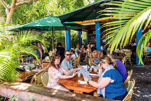 Key West, USA - May 1, 2018: People eating food at tropical restaurant tables jungle style tourists in Florida on travel, sunny day, bar called Blue Macaw Island Eats
