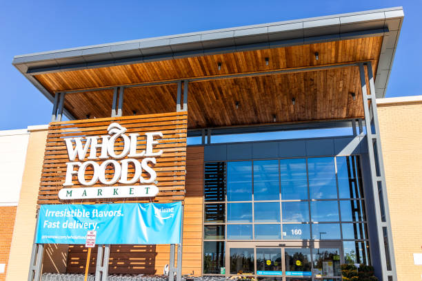 New, modern, large Whole Foods Market sign on exterior building in city in Virginia with people, blue Amazon Prime delivery sign, entrance Ashburn, USA - October 19, 2018: New, modern, large Whole Foods Market sign on exterior building in city in Virginia with people, blue Amazon Prime delivery sign, entrance ashburn virginia stock pictures, royalty-free photos & images