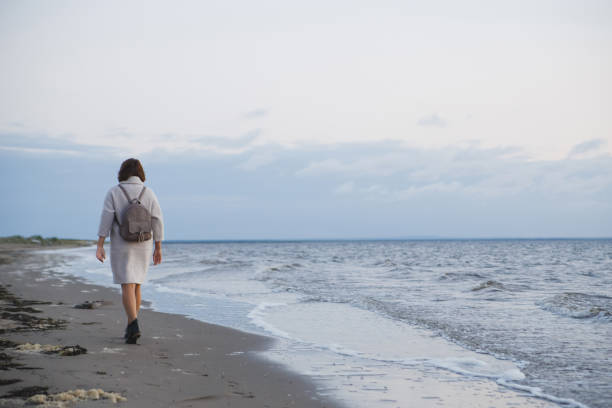 istock Woman in coat walking on the seashore 1131406142