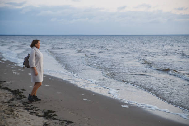 istock Woman in coat walking on the seashore 1131406144