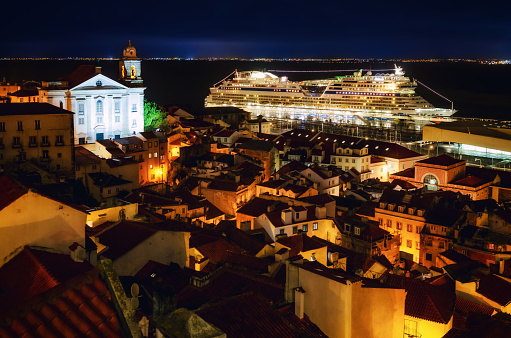 Night view of Lisbon (Portugal) cruise ships port from the miraduro of Santa Luzia, belvedere terrace over the streets of Alfama District, with the church of Santo Estevao