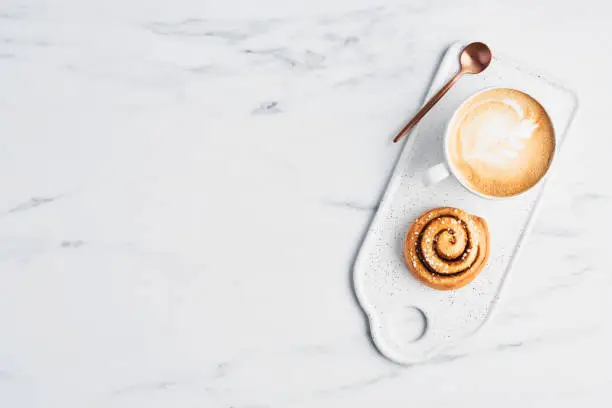 Photo of Freshly baked cinnamon roll and coffee with latte art