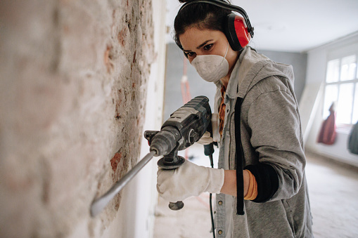 Young woman using drilling machine during reconstruction of her apartment