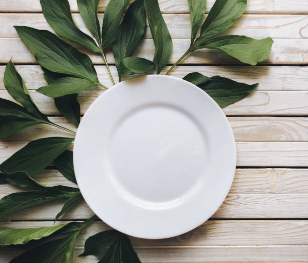 istock Empty white plate on light gray rustic wooden background with green leaves of peony. Copy space. 1131422096