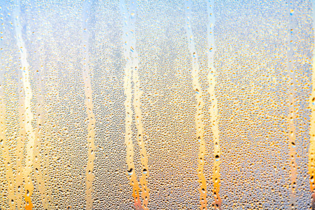 Abstract closeup pattern on rain or dew water drops on window and blue red orange vibrant colors during sunrise or sunset