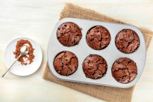muffin al cioccolato in uno stampo da forno, girato dall'alto con cacao in polvere e un posto per il testo - vegan food cake muffin chocolate foto e immagini stock