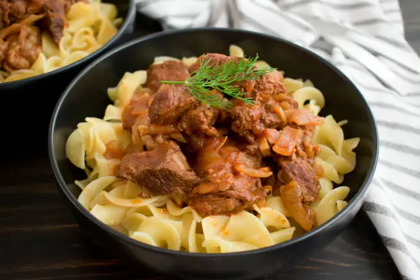 Bowls of garnished beef goulash over egg noodles