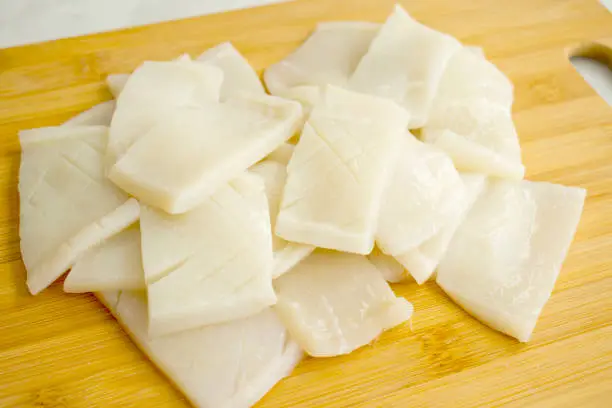 Scored slices of raw squid on a bamboo cutting board