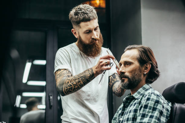 istock Calm bearded barber standing next to the client and holding comb 1131438889