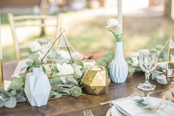 ambientazione da tavolo per una festa evento o un ricevimento di nozze, decorata con vasi di forma geometrica, candele d'oro rami e fiori di eucalipto. - plate dinning table blue foto e immagini stock