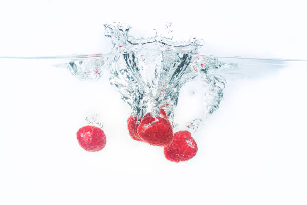 istock Bunch of raspberries splashing into water surface and sinking. Isolated on white background, splash food photography. 1131458883