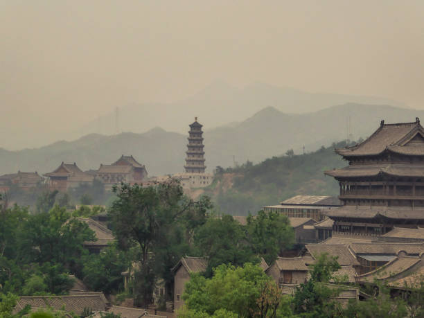 A polluted city of China, in the nearby of a Great Wall, a thick fog covers everything. Visibility is really low. Mountains barely visible. Tall temple in the middle. Traditional Chinese architecture