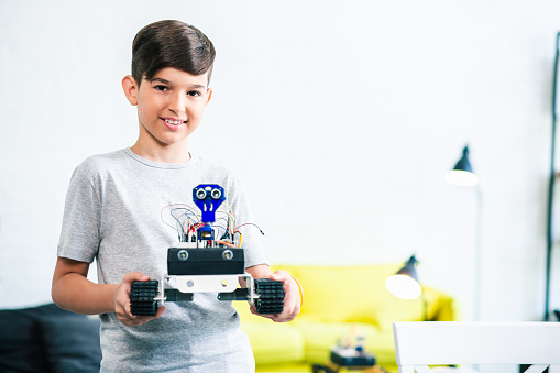 Cheerful nice little boy holding a robot while preparing for engineering competition