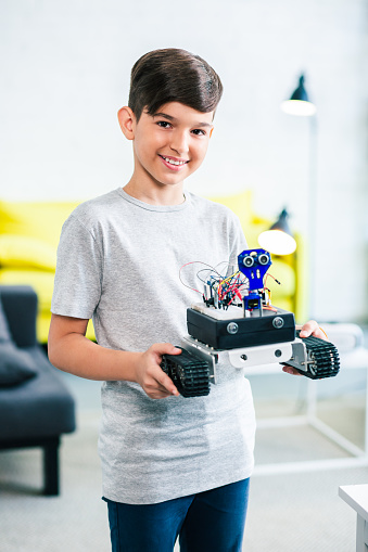 Nice smiling smart boy holding a modern robot done by him for engineering competition