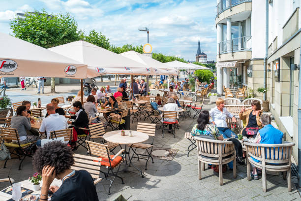 People enjoy the patio of a cafe-restaurant on the Rhine River promenade in Altstadt, downtown Dusseldorf,  North Rhine-Westphalia, Germany.