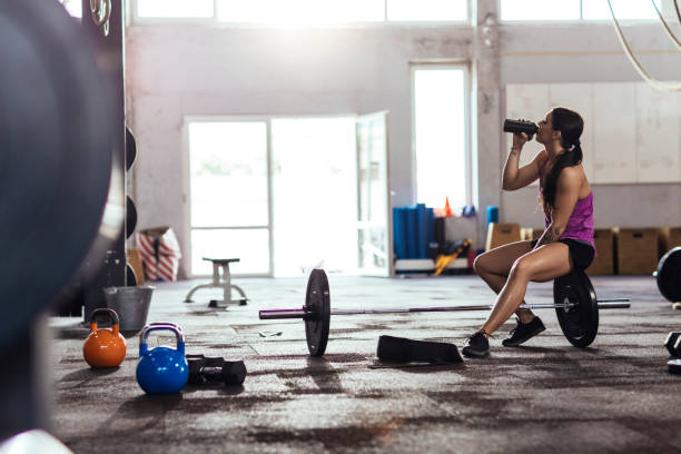 Training in the gym Girl resting and drinking water after weightlifting in the gym Barbell stock pictures, royalty-free photos & images