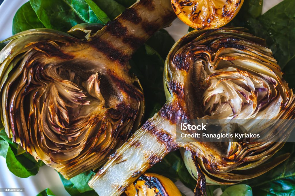 Grilled artichokes Grilled artichokes on a bed of spinach with grilled lemon halves Artichoke Stock Photo