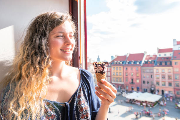 donna che tiene in mano un cono gelato al gelato al cioccolato alla vaniglia con sfondo a varsavia, polonia vecchio mercato piazza edifici storici in città durante la soleggiata giornata estiva - warsaw old town square foto e immagini stock