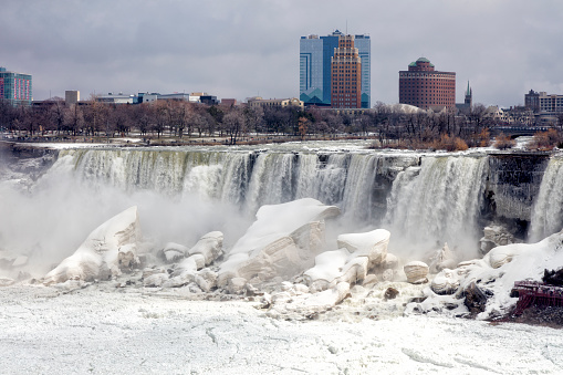 Niagara Falls on a cloudy day during winter, mist rising, USA, City of Niagara Falls in the background, view from Canadian side.
