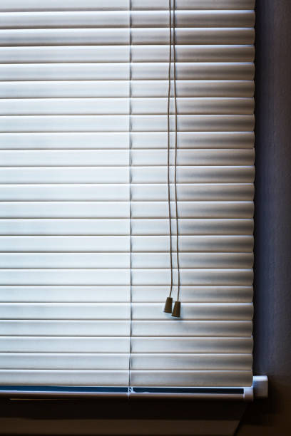 Closed, lowered, grainy venetian blinds cover a mysterious window in a dark, spooky room.