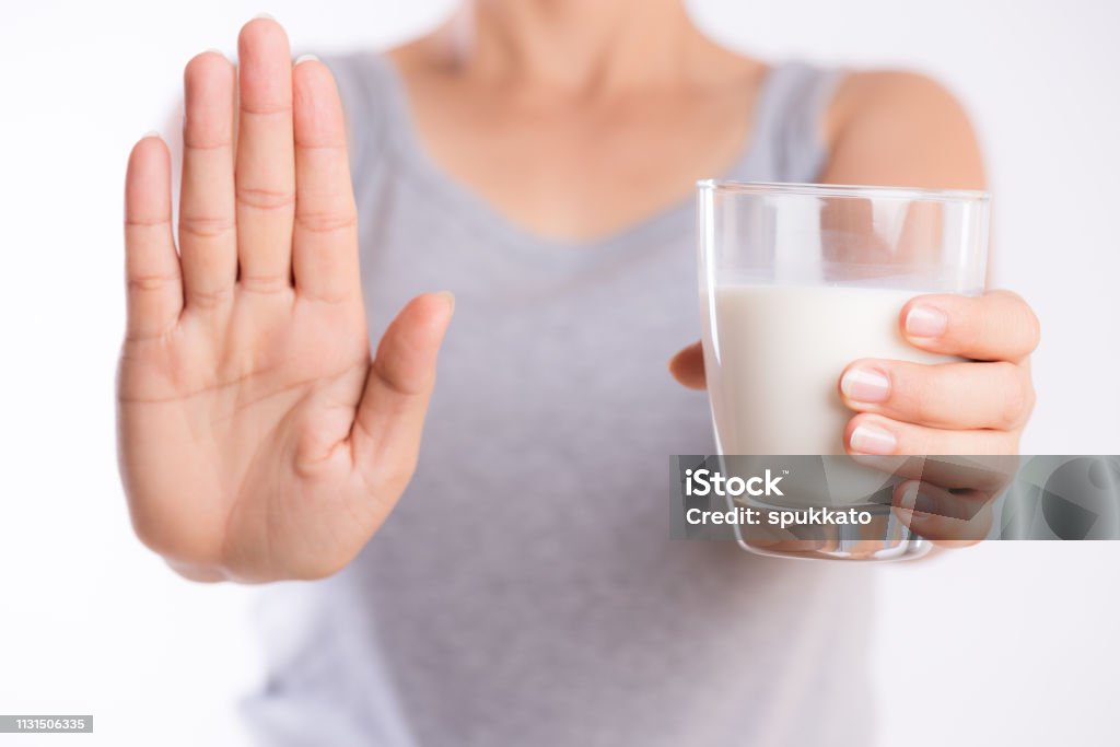 Frau Hand hält Glas Milch mit schlechten Magenschmerzen wegen Laktoseintoleranz und eine andere Hand zeigt Stoppschild. Gesundheitsproblem mit Milchprodukten, Gesundheitsfürsorge und medizinischem Konzept. - Lizenzfrei Vorurteil Stock-Foto