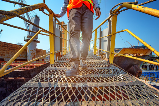 legs of worker or engineering wearing Safety shoes walking in mind step on the steel gangway bridge cross over at workplace, working in high stage and high level of insurance