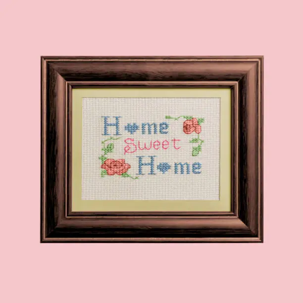 A traditional home sweet home sampler in a frame against a pink background.