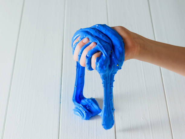 istock The blue slime flows from the child's hand onto the white table. 1131515312