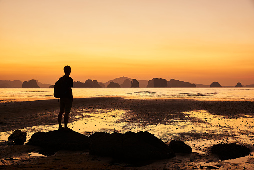 A man standing on the rock on the beach looking at beautiful sky before sunrise at Koh Yao Noi, Phangnga province, Thailand